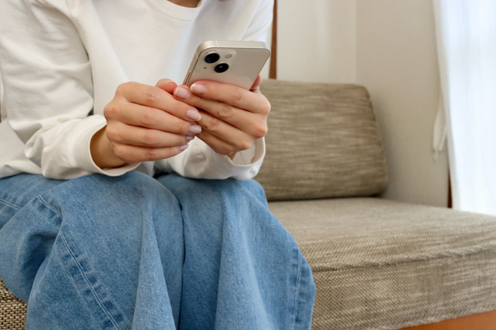 ソファーに座ってスマートフォンを持っている女性の写真