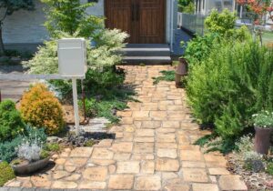 ベージュ系のレンガでできたアプローチと緑の植物が生えている、白いポストが印象的な庭