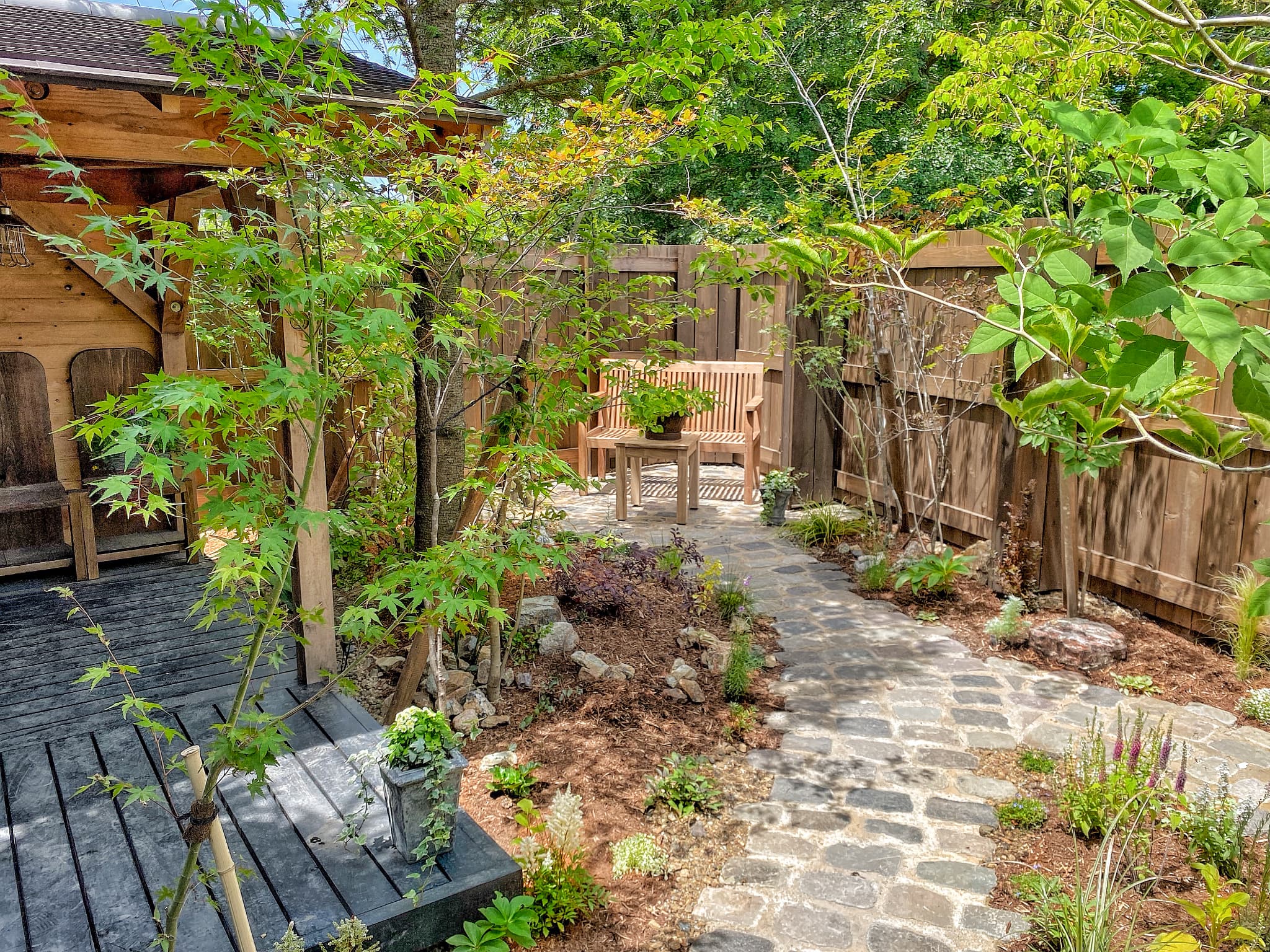 石で作られたアプローチ、木製のスツールとベンチ、植物が生えた庭